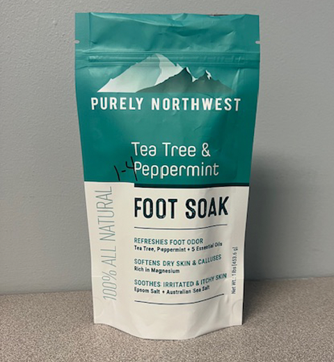 A stand-up pouch labeled "Purely Northwest Tea Tree & Peppermint Foot Soak." It claims to refresh foot odor, soften dry skin and calluses, and soothe irritated skin. The packaging is teal and white with a mountain logo.